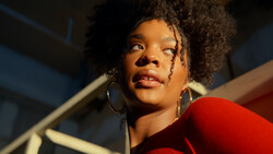 Woman with natural curly hair wearing hoop earrings and red clothing, looking upward in dramatic studio lighting.