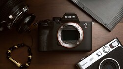 Sony a7 mirrorless camera body with interchangeable lenses and vintage film camera arranged on brown surface.