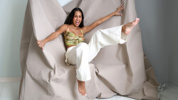 Woman in gold and white outfit performing dynamic aerial pose against draped beige fabric backdrop.