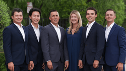 Six professionals in business attire posed against a green foliage backdrop.
