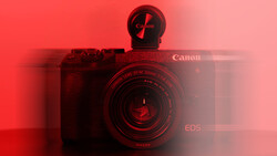 Canon EOS camera with telephoto lens against a red gradient background with directional lighting.