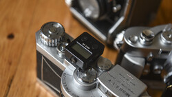 Vintage rangefinder camera with light meter attachment mounted on top, alongside other classic cameras on wooden surface.