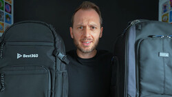 Man standing between two large black camera backpacks against a dark background.