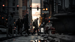 Urban street at dusk with wet pavement reflecting neon signs and city lights.