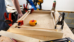 Woodworking workbench with tools, clamps, and a wooden project in progress.