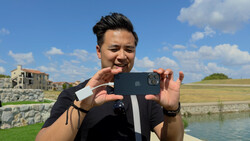 Photographer holding smartphone horizontally to capture landscape scene with water and countryside.