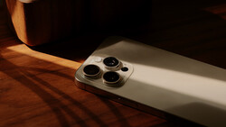 Silver smartphone with triple camera system positioned on warm-toned wooden surface with dramatic side lighting.