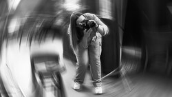 Photographer holding camera to face, captured with radial motion blur effect creating dynamic swirling background.