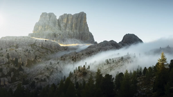 Dramatic mountain peak with columnar rock formations shrouded in rolling mist above a forested valley.