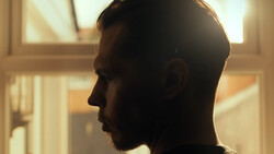 Man in profile silhouette backlit by warm window light, showing contemplative expression.