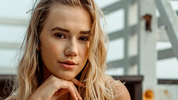 Young woman with blonde wavy hair resting her chin on her hand, gazing directly at the camera with a contemplative expression.