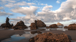Rocky outcrops and tidal pools on a sandy beach under a dramatic cloudy sky.