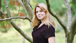 Young woman with blonde hair leaning against a tree branch in natural outdoor setting.