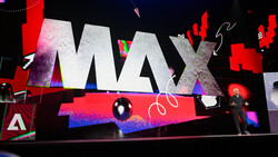 Large-scale conference stage display with bold MAX typography and vibrant neon pink and blue lighting effects.