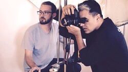 Two photographers examining a Canon camera in a studio setting with white walls and professional lighting.