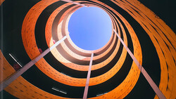 Concentric circles of terracotta brick spiraling upward toward bright blue sky through a cylindrical opening.