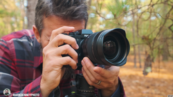 Photographer holding a camera with wide-angle lens, composing a shot in an autumn forest setting.