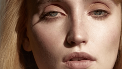 Close-up portrait of a woman with blonde hair and neutral expression, lit with soft, directional light creating subtle shadows.