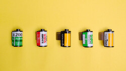 Five vintage film canisters arranged in a row against a bright yellow background.