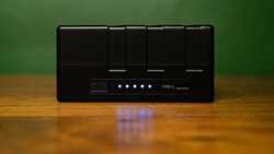 Black USB hub with five glowing blue LED indicator lights mounted on wooden surface against green background.