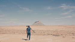 Person standing in vast desert landscape pointing toward distant mountain peak.
