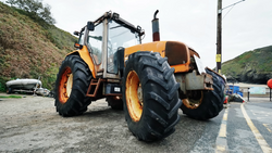 Orange and black heavy machinery tractor with large treaded tires parked on an asphalt road beside a hillside.