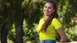 Woman in bright yellow t-shirt smiling at camera with trees in background.