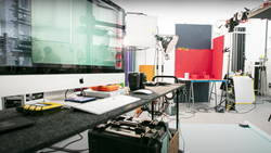 Professional photography studio workspace with Mac monitor, lighting equipment, and red backdrop panels.