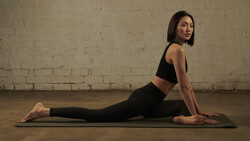 Woman performing upward-facing dog yoga pose on a mat against an industrial brick wall.