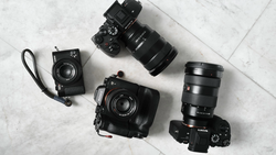 Collection of four black cameras and lenses arranged on a marble surface.