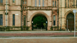 Large arched entrance of a historic stone building with manicured shrubs visible through the opening.