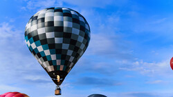 Black and white checkered hot air balloon floating against a blue sky with wispy clouds.