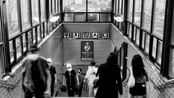 Blurred commuters moving through a subway station stairwell with Korean signage and brick walls.