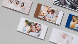 Collection of printed photo books and albums arranged on a gray surface, displaying various family portraits and lifestyle photography.