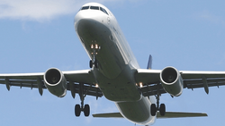 Commercial aircraft approaching for landing with landing gear deployed against blue sky.