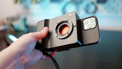 Hand holding a smartphone with an attached macro lens accessory and LED ring light module.