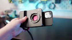 Smartphone with external lens attachment and macro lens adapter held in hand.