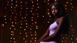 Woman in lavender tank top posed against warm bokeh lights in dark background.