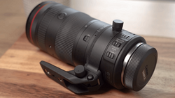 Black telephoto lens with red ring mounted on wooden surface with black camera strap.