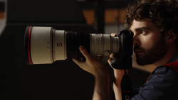 Photographer holding a telephoto lens camera up to his eye, composing a shot in dramatic side lighting.