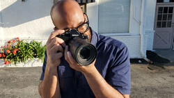 Photographer holding a Nikon DSLR camera with telephoto lens in bright outdoor sunlight.