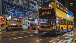 Double-decker buses on a Hong Kong street at night with illuminated buildings and advertisements in the background.
