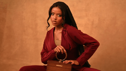 Woman in burgundy blazer posing with wooden box against warm tan backdrop.