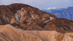 Layered desert mountains with warm earth tones, snow-capped peaks visible in the distance.