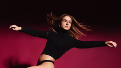 Woman in black crop top and high-waisted bottoms posed dynamically against deep magenta background with arms extended.