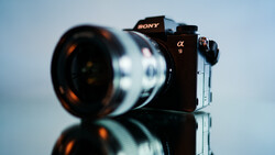 Sony α9 mirrorless camera with telephoto lens mounted, photographed against a neutral sky background with reflective surface below.