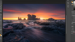Dramatic coastal landscape with rock formations silhouetted against vibrant orange and purple sunset sky.