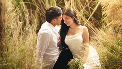 Couple embracing in a field of tall dried grasses during golden hour.