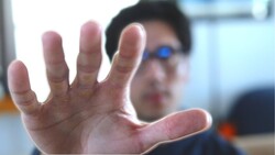 Person's open hand raised toward camera in close-up shot with blurred background.