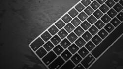 Overhead view of a silver and black wireless keyboard on a dark textured surface.